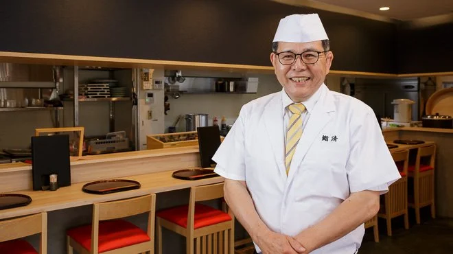 木のカウンター席と落ち着いた照明がある寿司店の店内全景